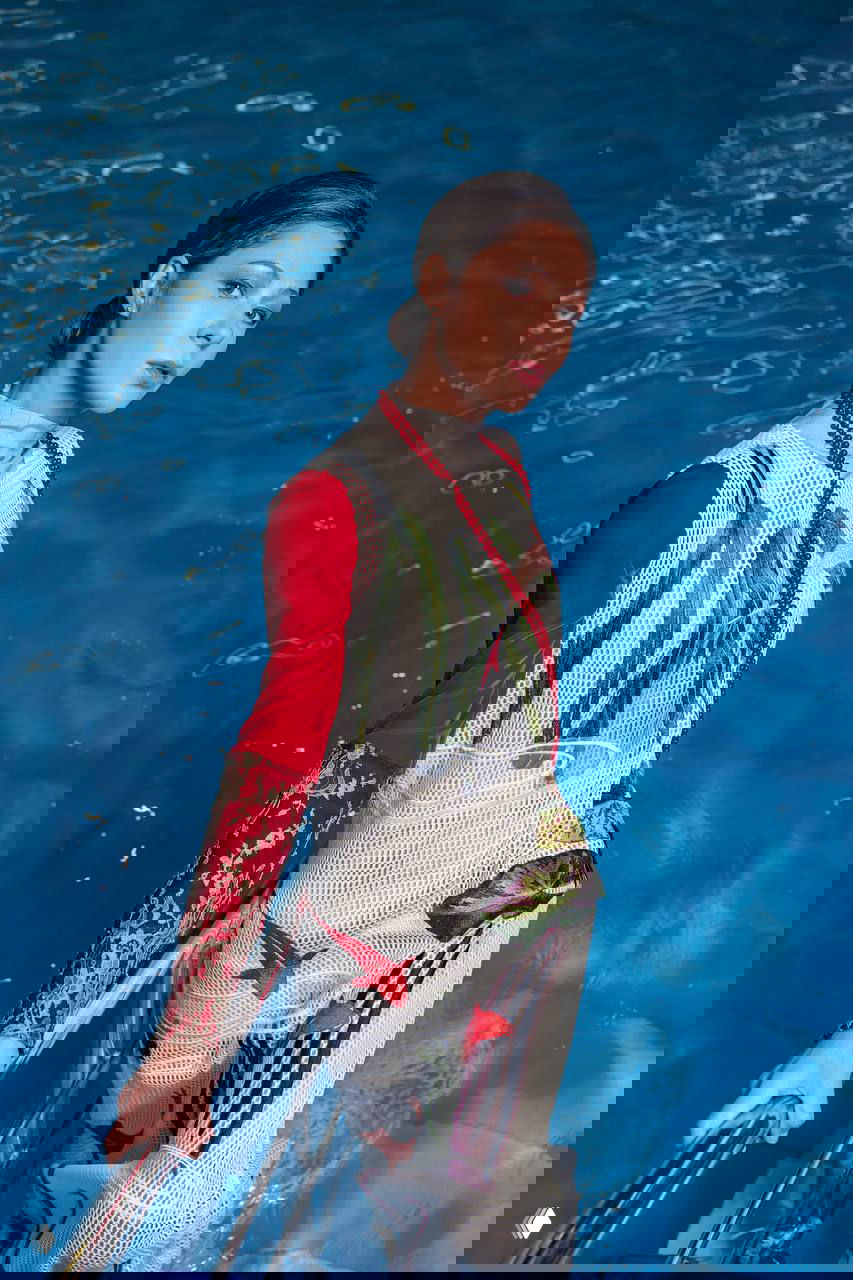 Портрет женщины в декоративном платье у края бассейна: насыщенный синий фон воды и элегантная поза в фотосете.