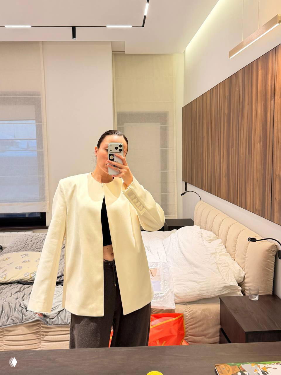 Селфи женщины в зеркале спальни особняка: кровать с мягким изголовьем, деревянные панно на стене и минималистичный интерьер комнаты.