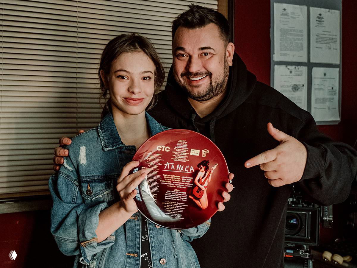 Ника Жукова вместе с Сергеем Жуковым держат памятную виниловую пластинку проекта «Плакса», оба улыбаются в гримерной зоне после мероприятия.