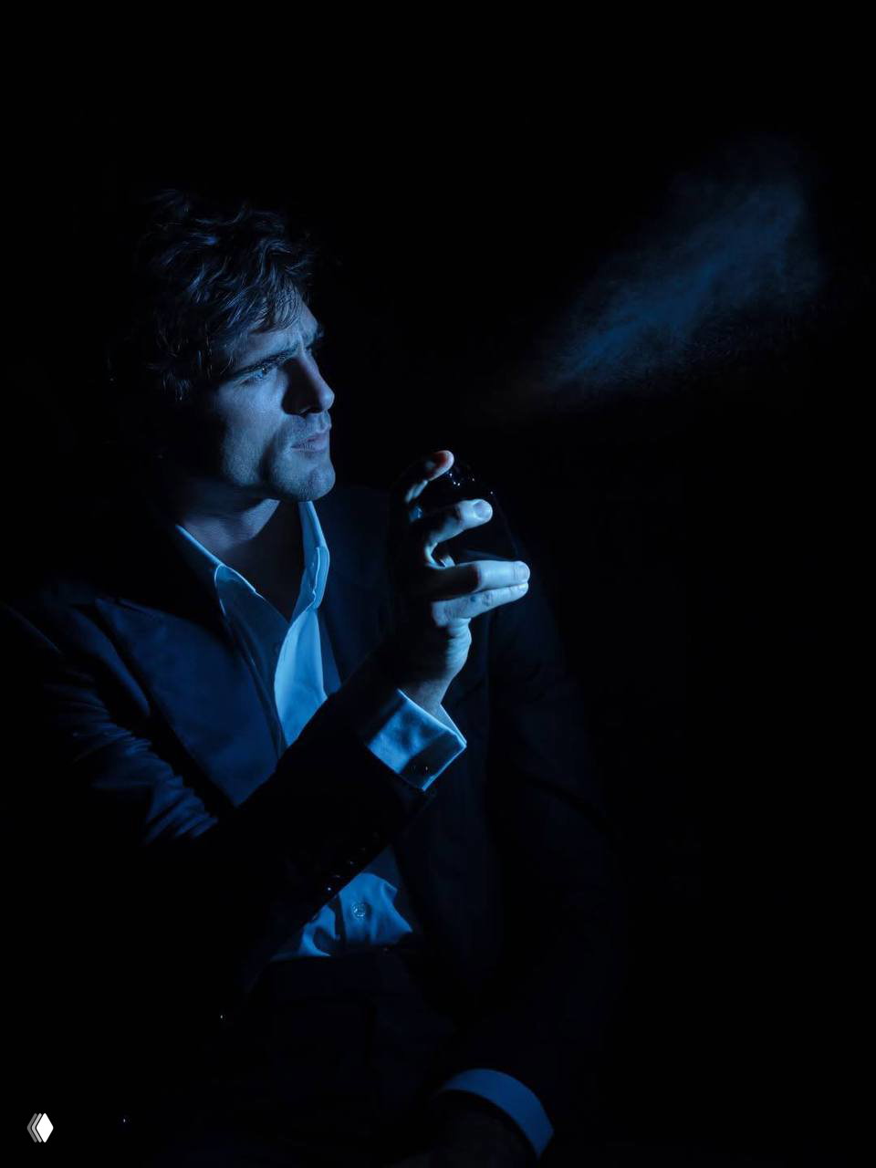 Мужчина в костюме снят в третьем плане на синем фоне — расслабленная поза в студии, стильная рекламная фотография.