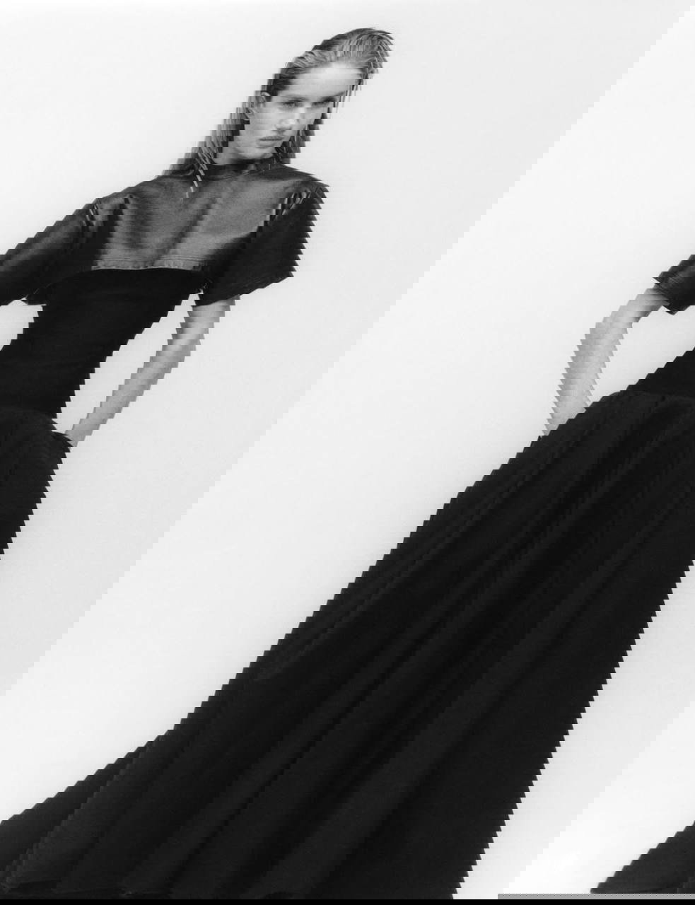 Чёрно‑белый полноформатный кадр супермодели в корсетном наряде и длинной юбке, строгая поза и классическая студийная постановка.