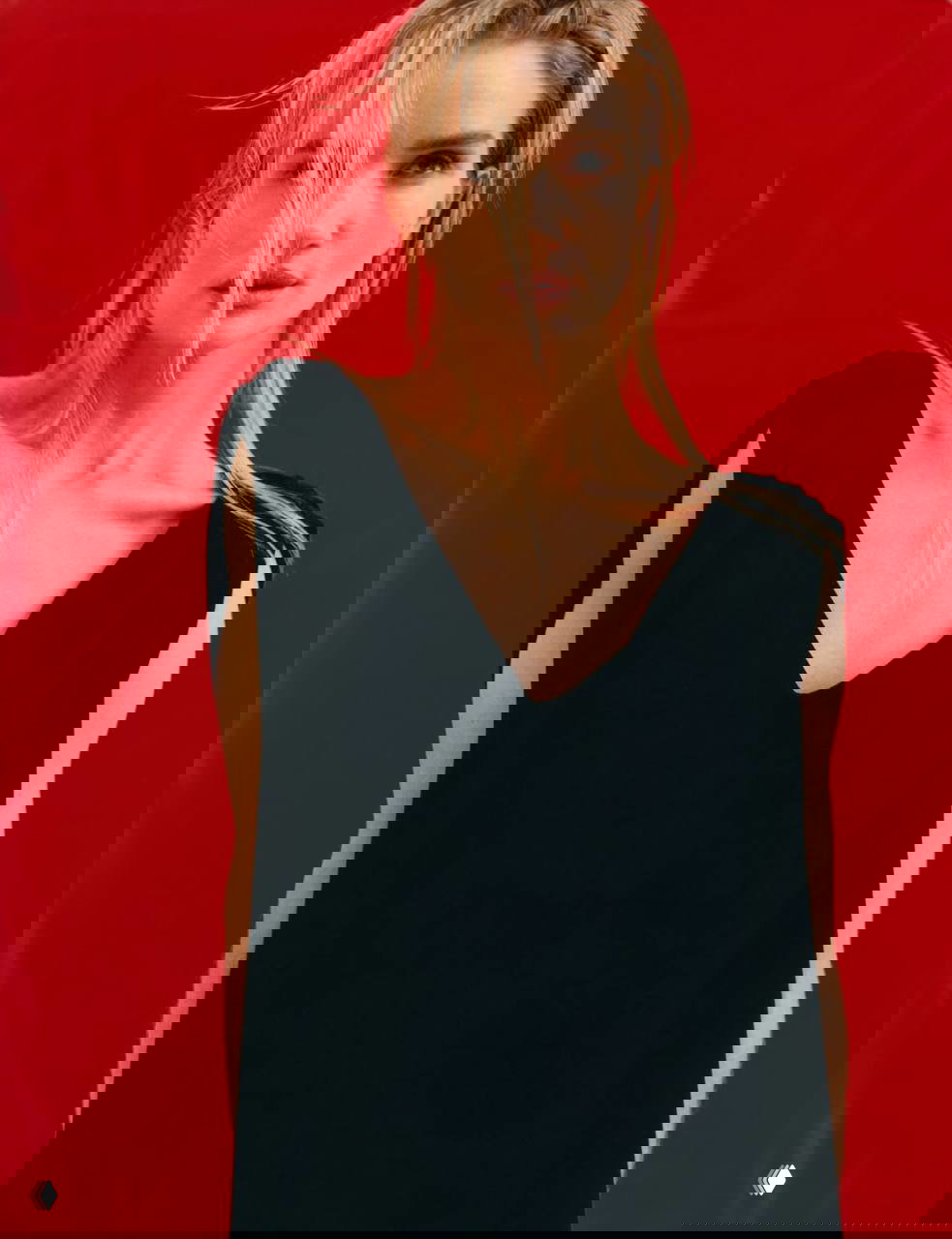 Крупный портрет модели на красном фоне в свободном чёрном платье: акцент на чертах лица и реминисценция модной эстетики.