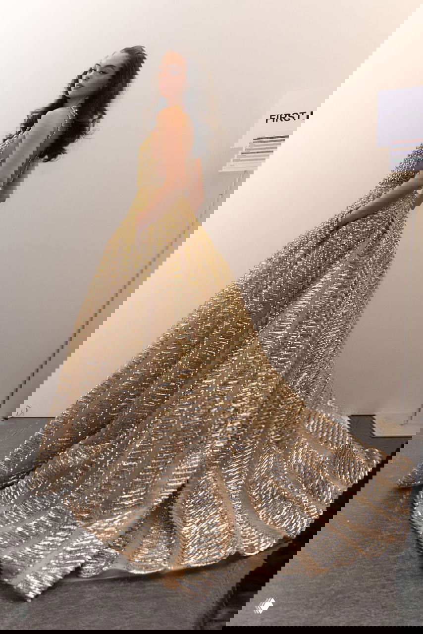 Вид со спины на длинное золотое кутюрное платье с шлейфом в гримерной или бэкстейдж зоне показа