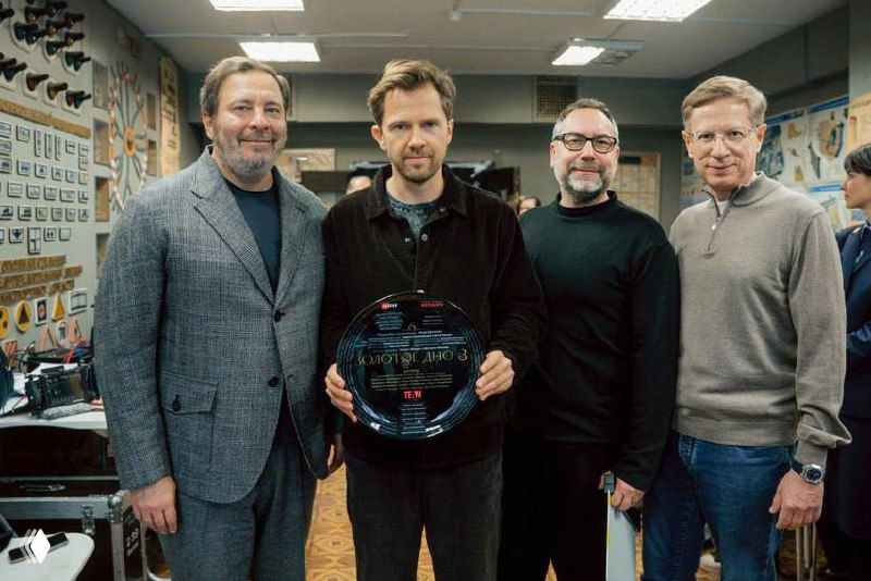 Размытый и артефактный кадр с группой людей на фоне интерьера: диагональные искажения, видны фигуры и предметы мебели частично.