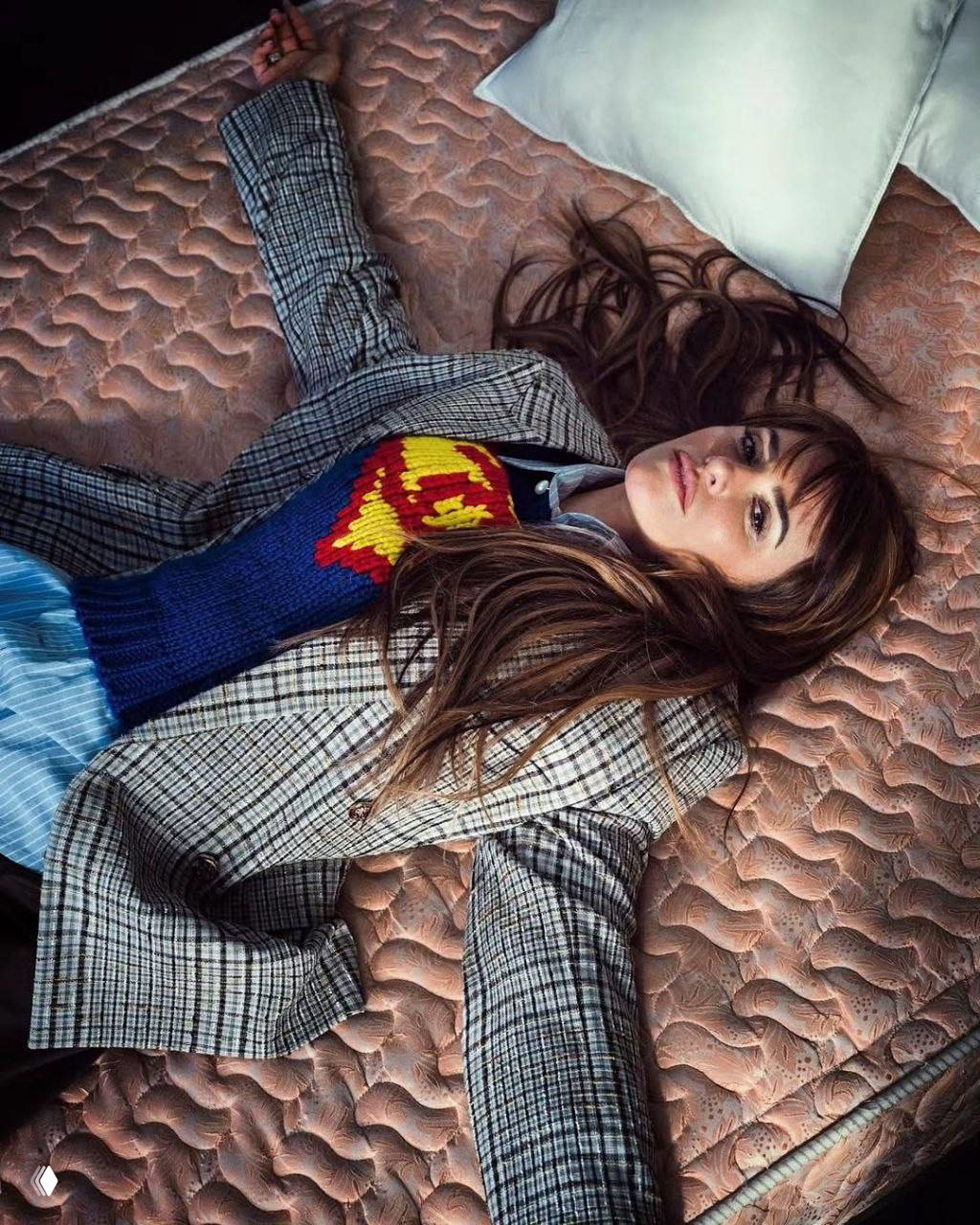 Верхний ракурс: женщина лежит на матрасе в клетчатом пиджаке и вязаном свитере; образ и поза подчёркивают концепцию модной съёмки в студии.