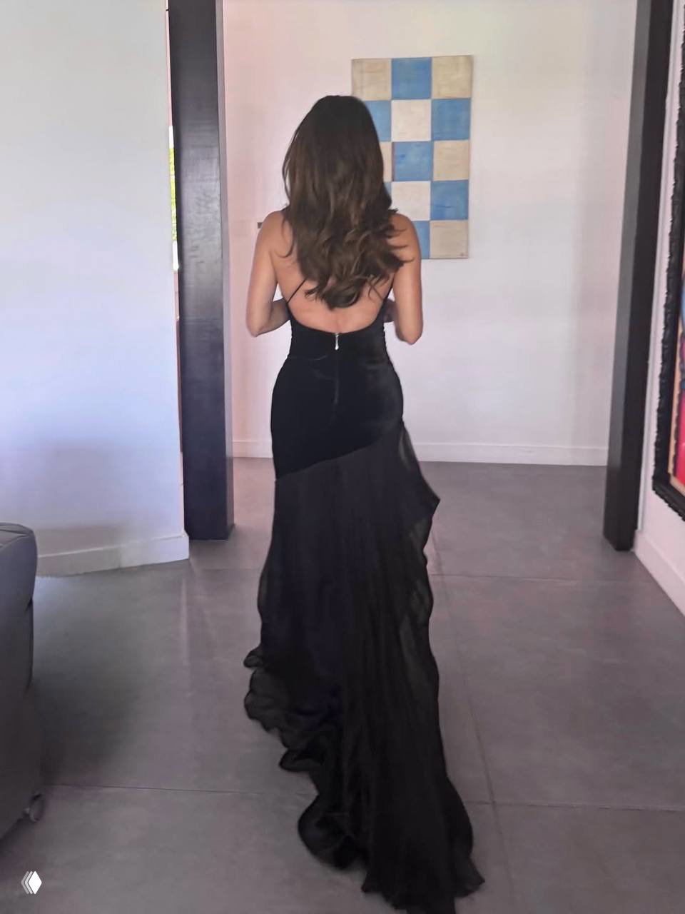 Обратный ракурс: женщина в чёрном платье с открытой спиной и длинным шлейфом идёт по интерьеру, видна драпировка ткани по полу.