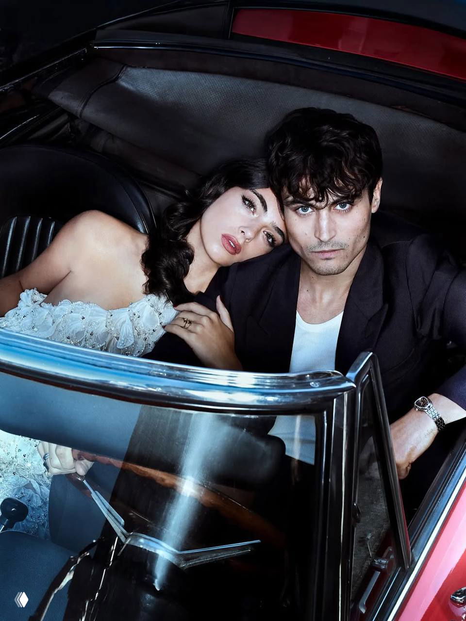 Крупный план пары в салоне машины: женщина в светлом платье и мужчина в пиджаке смотрят в камеру, модный фоторепортаж с глянцевым оформлением.