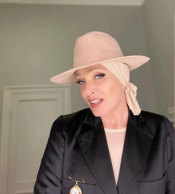 Современный портрет в шляпе и платке: Лайма Вайкуле в стильном образе, интерьерное фото с мягким светом и лёгкой улыбкой.