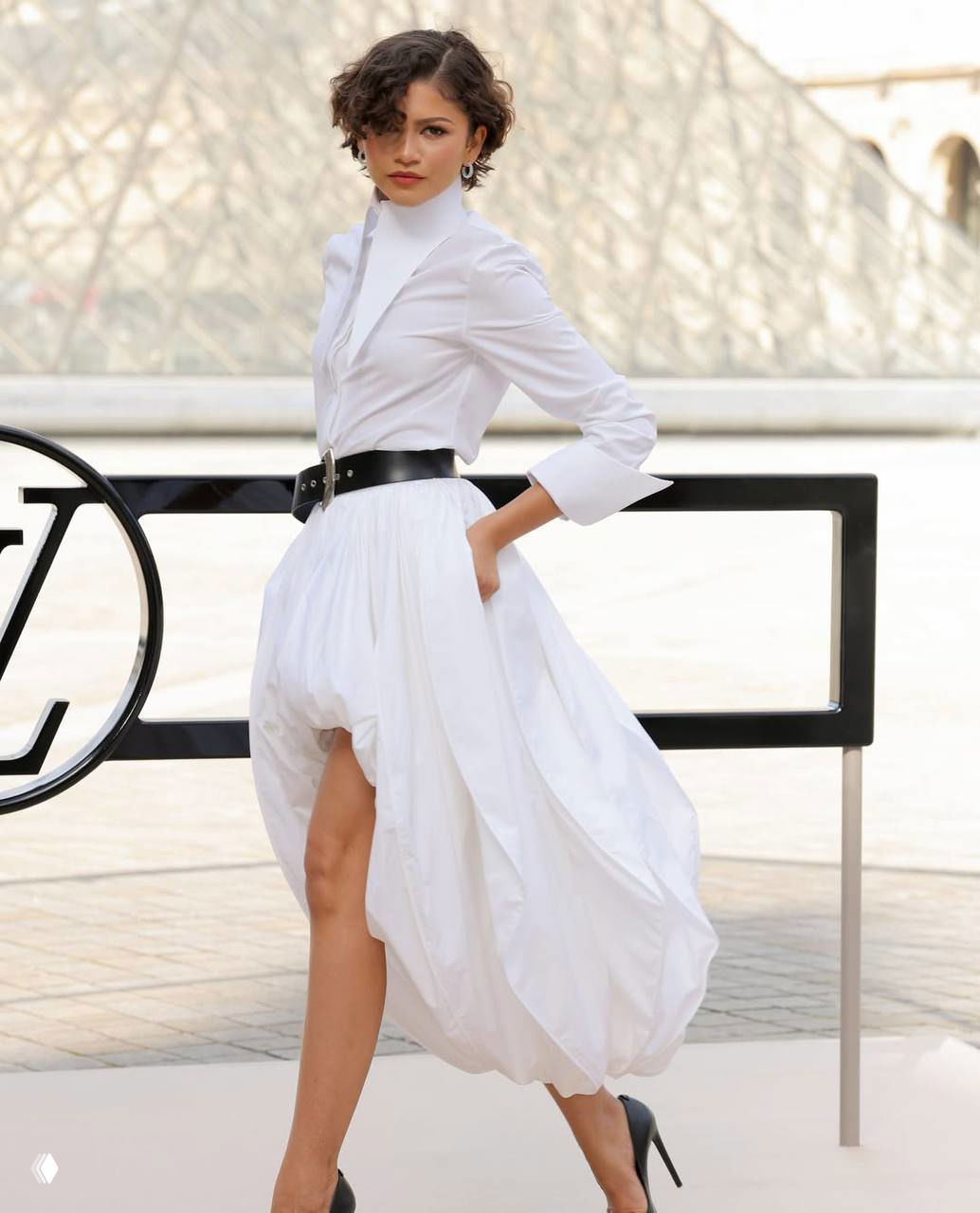 Модель в белом пышном платье с чёрным поясом на показе Louis Vuitton в Париже — ракурс в полный рост у подиума.