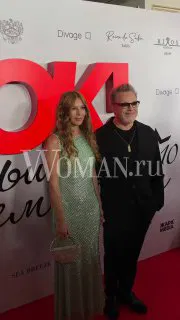 Дуэт в вечерних образах стоит у фонового логотипа мероприятия OK! Awards; крупный план, заметна фотозона с брендами и водяной знак.