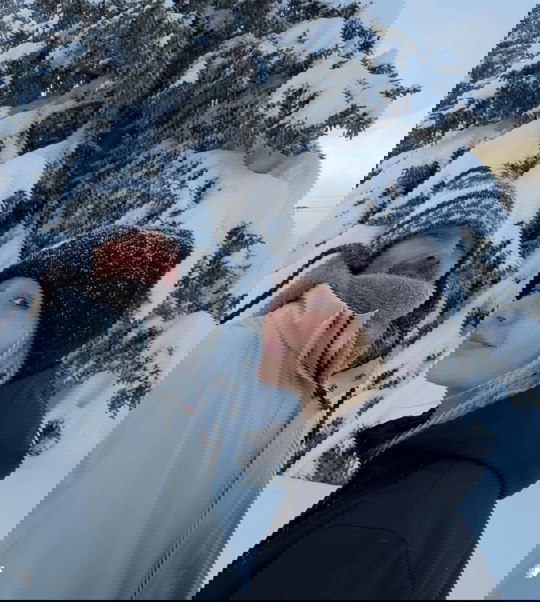 Дэвид Бекхэм и Харпер на прогулке в заснеженном лесу в тёплой одежде; на заднем плане крупные заснеженные ели и зимний пейзаж.