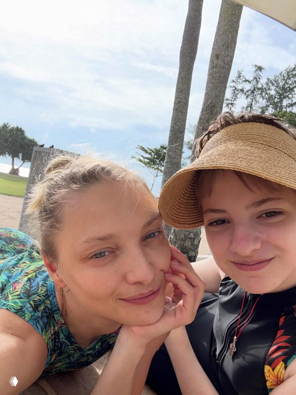 Женщина и подросток в шляпе на пляже: крупный план с пальмами и морским пейзажем на заднем плане, солнечная обстановка.