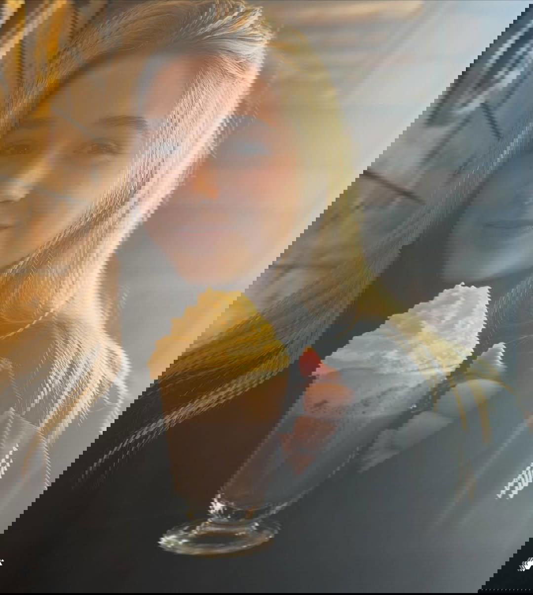 Харпер держит кружку с горячим напитком и взбитыми сливками в кафе; тёплое освещение и деревянный интерьер создают домашний уют.