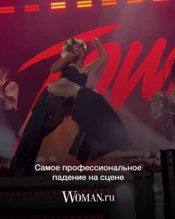 Катя IOWA падает на сцене во время концерта; артистка в сценическом костюме при ярком световом оформлении, запечатлён динамичный момент падения.