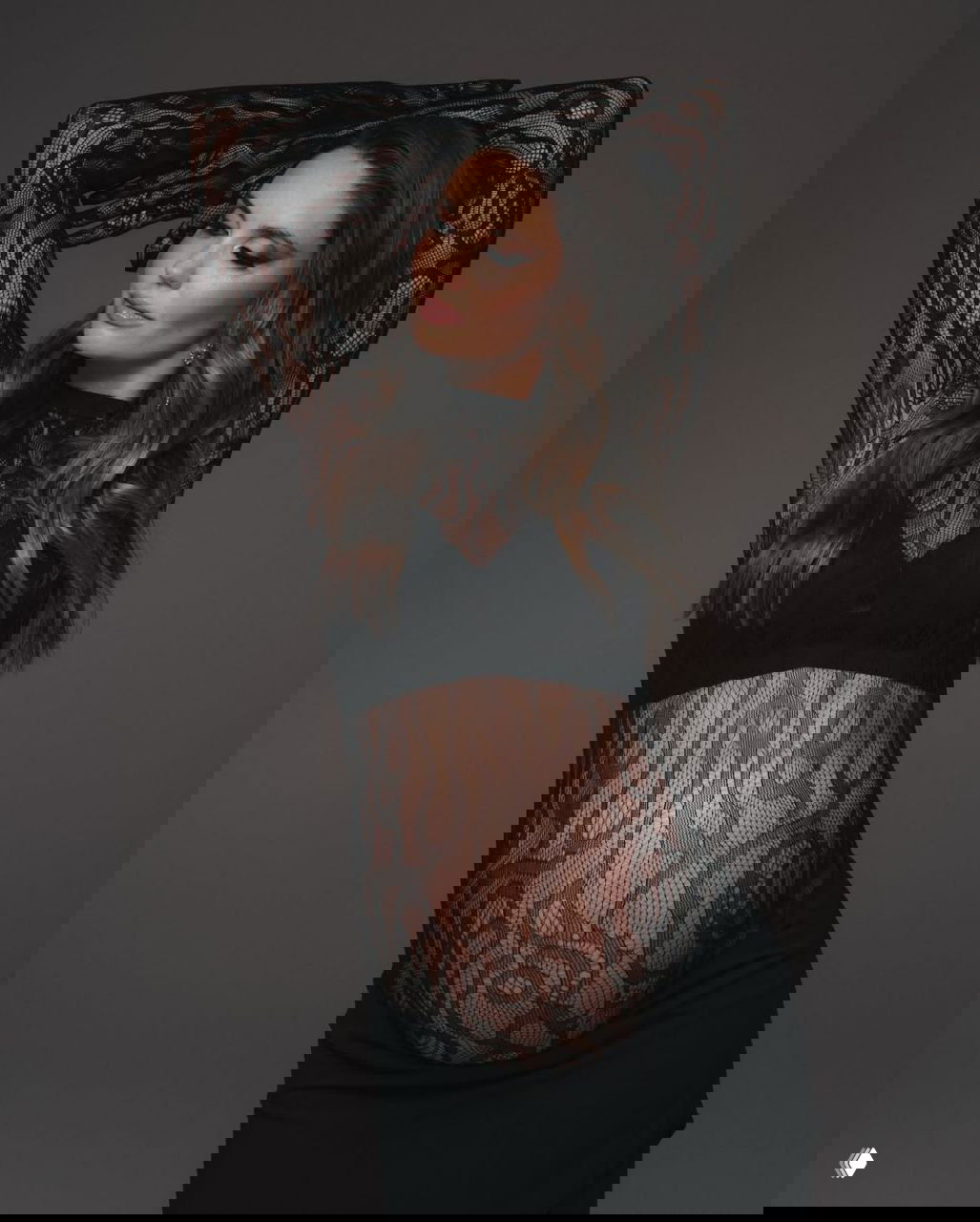 Портрет Агаты Муцениеце с руками над головой в кружевном комплекте, плавные волосы и макияж, студийный фон нейтрального тона