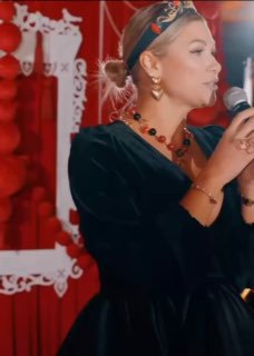 Женщина в чёрном платье с микрофоном на фоне красных украшений — кадр с празднования дня рождения супруги Вадима Галыгина.