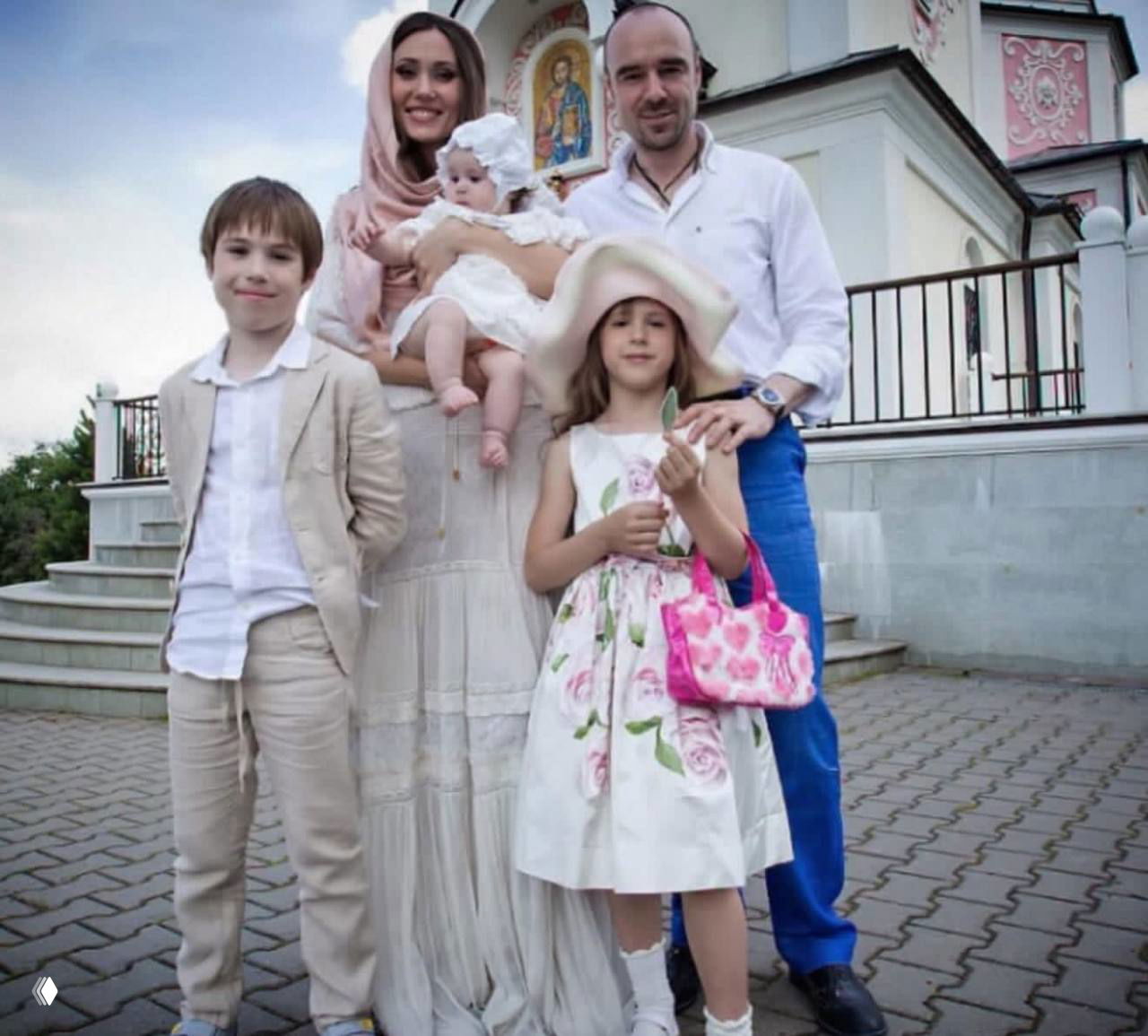 Архивное семейное фото на улице у здания церкви: родители позируют с несколькими детьми в светлой одежде в торжественной обстановке.