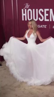 Кадр видео: женщина в пышном белом платье кружится на красной дорожке во время премьеры фильма «Горничная», виден объемный подол.