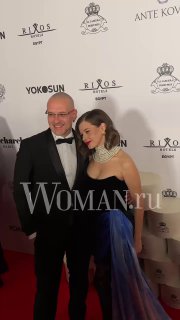 Ещё одна пара в вечерних образах на красной дорожке у фотозоны OK! Awards; на фото видно элементы декора и водяной знак WOMAN.ru.
