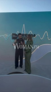 Ольга Воронцева беседует с участником на фоне арт-инсталляции Dream Fest в Баку; сцена и декор мероприятия видны за ними, логотип Woman.ru присутствует.