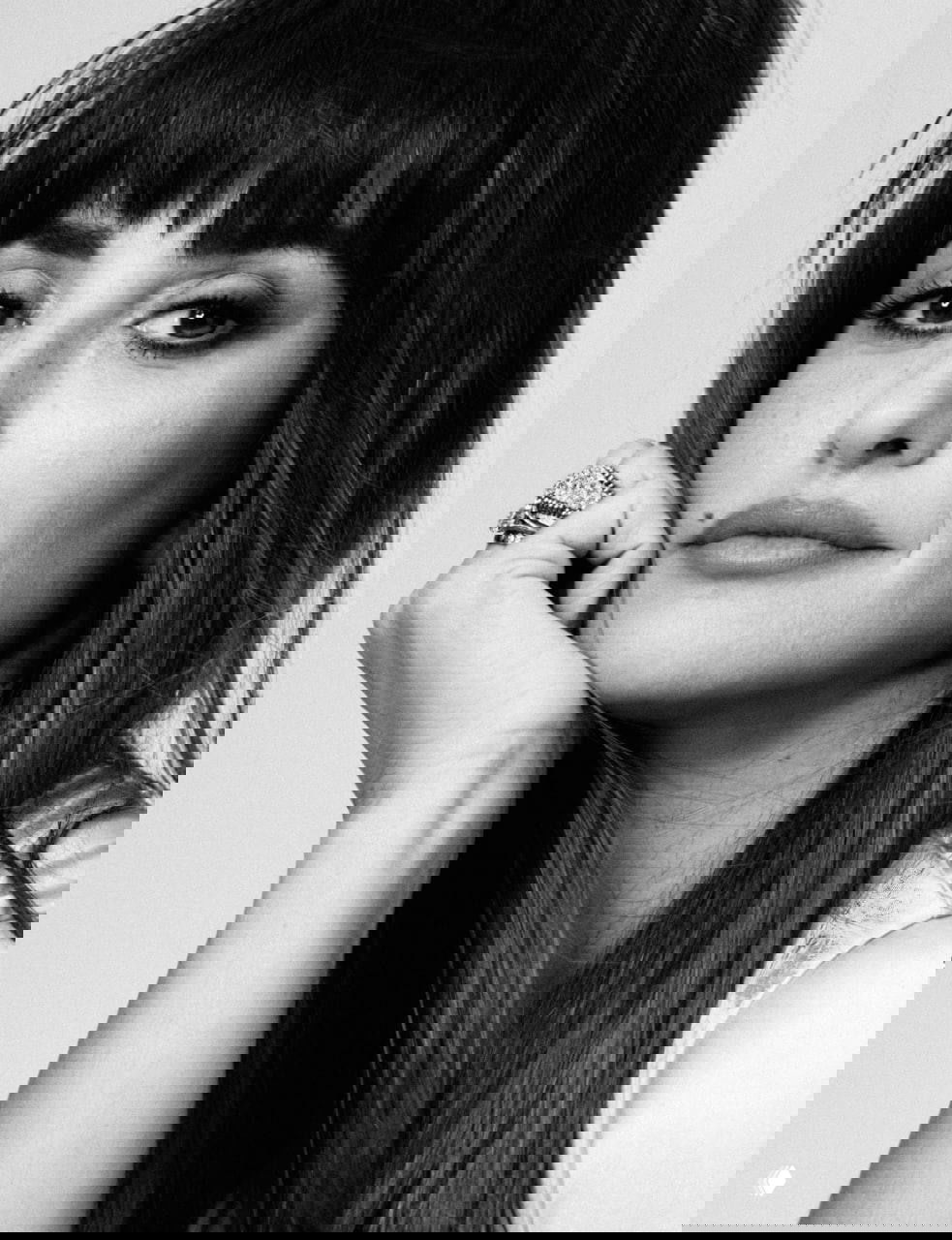 Чёрно‑белый портрет женщины в студии: опора подбородком на руку, акцент на глазах и деталях украшений, монохромная эстетика.