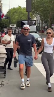 Мужчина и женщина идут по тротуару, держась за руки; мужчина в кепке, женщина в спортивной одежде, городская прогулка.
