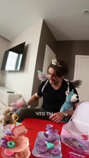 Мужчина в короне и с детскими игрушками сидит за столом с детским чайным набором — домашняя сцена к новости о песне «Колыбельная».