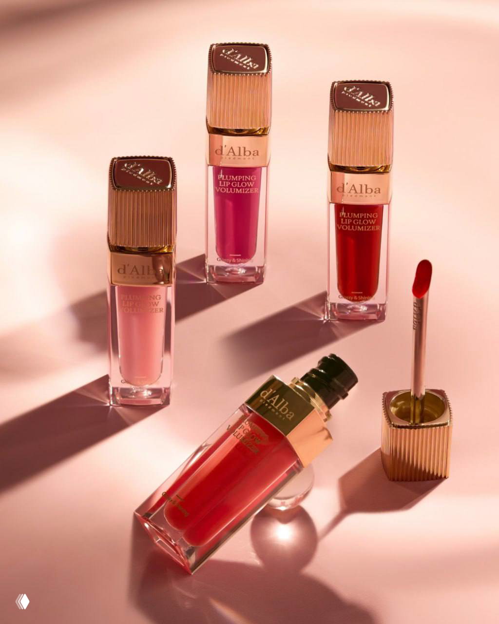 Несколько флаконов блесков d'Alba разложены на розовом фоне: разные оттенки, один открытый с видимым аппликатором