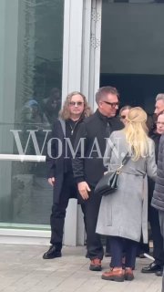 Несколько человек в тёмной одежде и солнечных очках выходят из здания, держа цветы — кадр с места прощания в Москве.