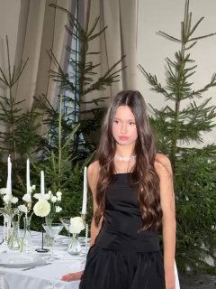 Девушка в черном платье у праздничного стола с белыми свечами и елочными ветками, оформленная как семейный фотокадр.