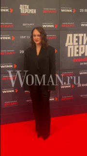 Аглая Тарасова на красной дорожке премьеры второго сезона «Дети перемен», в чёрном костюме на фоне баннера с логотипом Woman.ru.