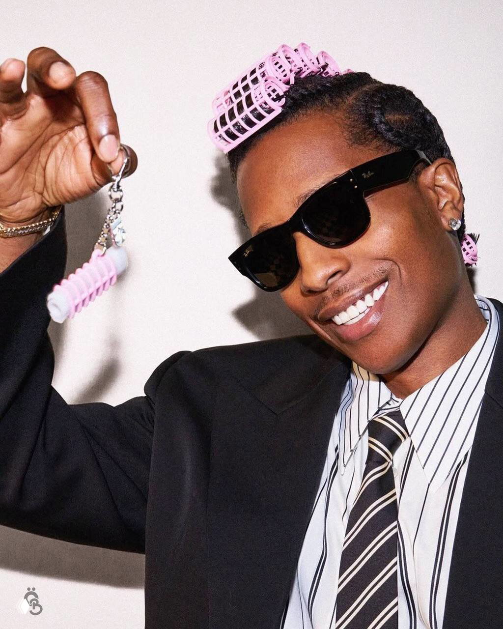 A$AP Rocky улыбается в очках и держит в руке брелок-бигуди и миниатюрный продукт Fenty Skin — кадр из промосъемки лимитированной коллекции.