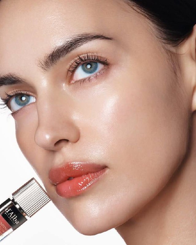 Крупный план области губ и части лица модели с глянцевым блеском, акцент на текстуре покрытия и отражениях света