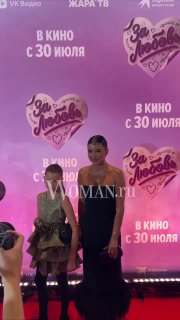 Женщина и девочка в нарядах стоят у баннера премьерного показа «За любовь»: розовый задник с логотипом фильма и надписью «В кино с 30 июля».