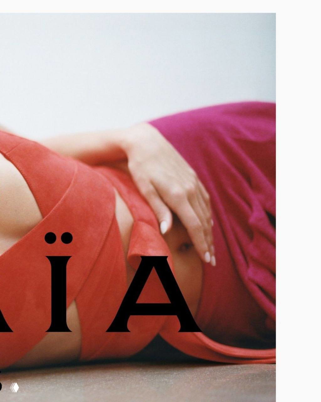 Кадр из той же рекламной серии Alaïa: модель лежит в красном наряде на светлом фоне, видны детали ткани и часть логотипа бренда.