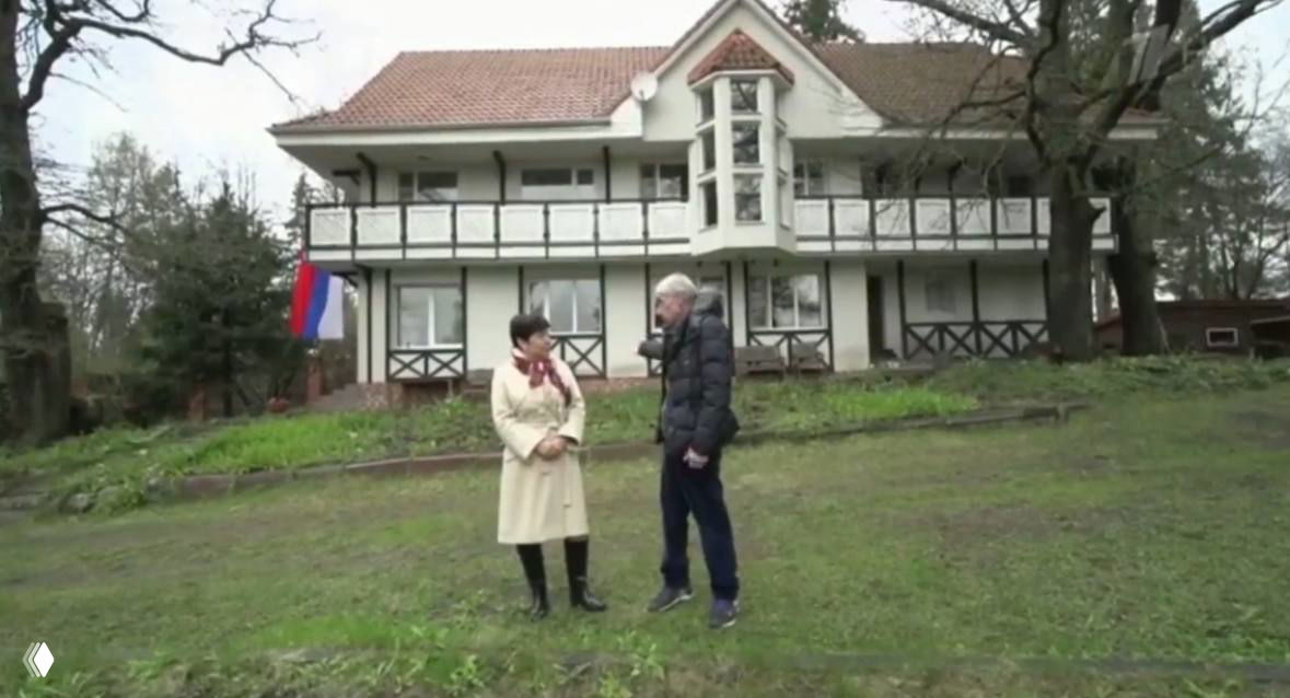 Загородный дом на Истре в кадре: двухэтажная усадьба с верандой и садом, на переднем плане стоят люди у дома, виднеется флаг у фасада.
