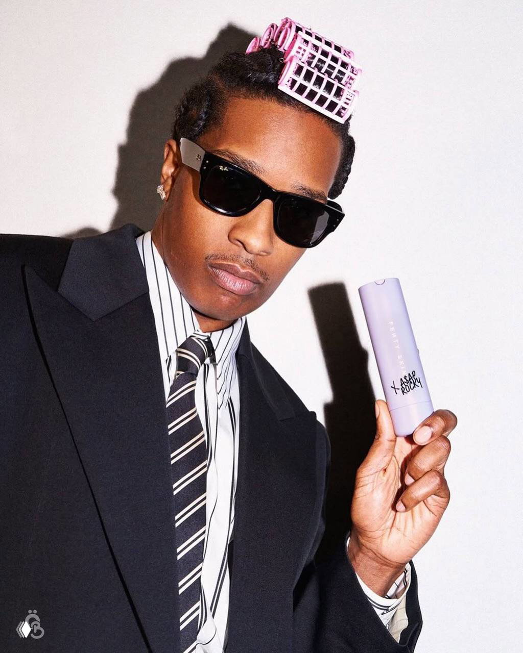 A$AP Rocky в строгом костюме демонстрирует цилиндрический флакон увлажняющего средства Fenty Skin x A$AP Rocky на светлом фоне рекламной сессии.
