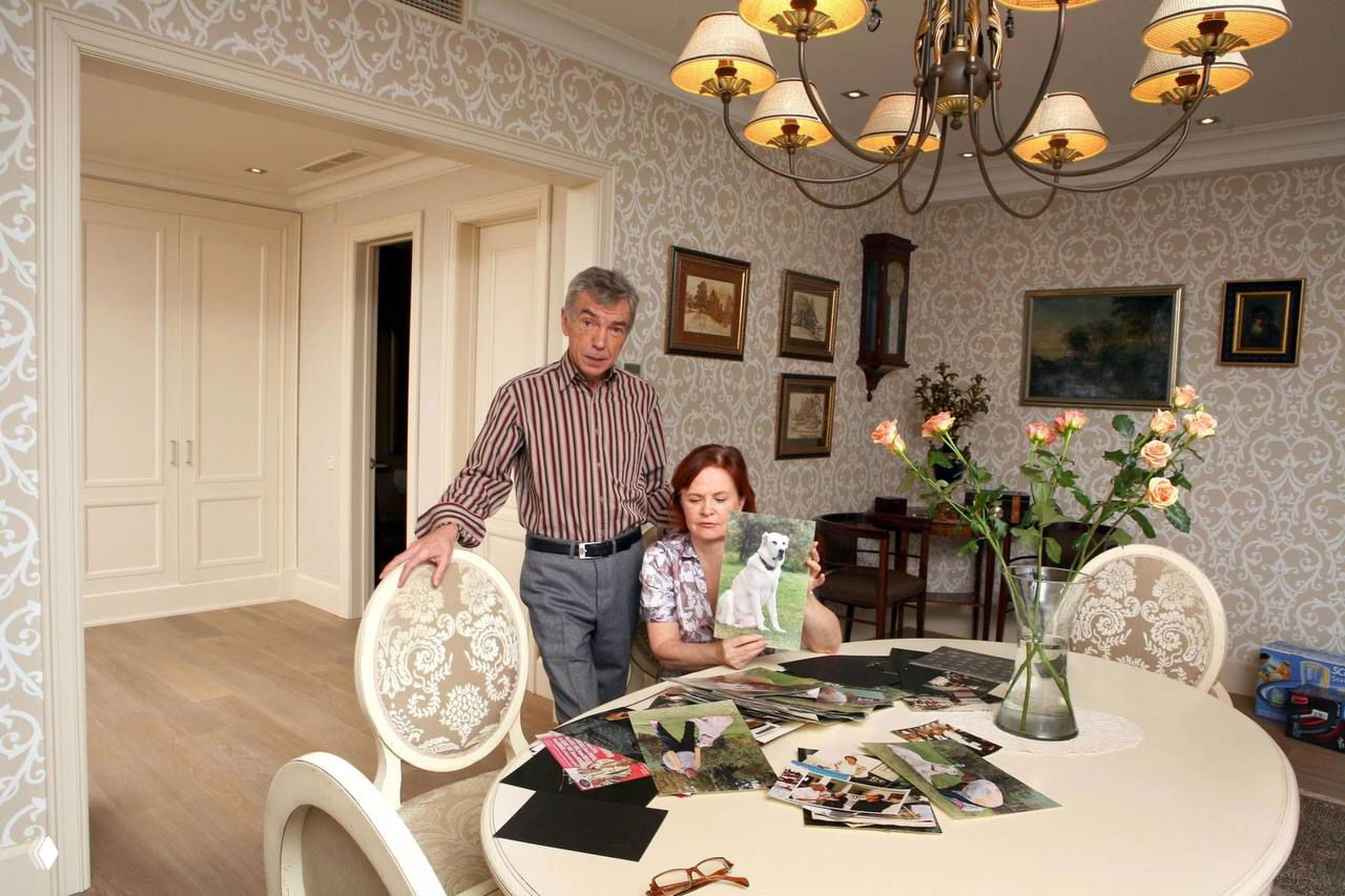 Юрий Николаев и женщина за круглым столом в светлой столовой: на столе фотографии и буклеты, рядом ваза с цветами, семейная обстановка в квартире на Саввинской.