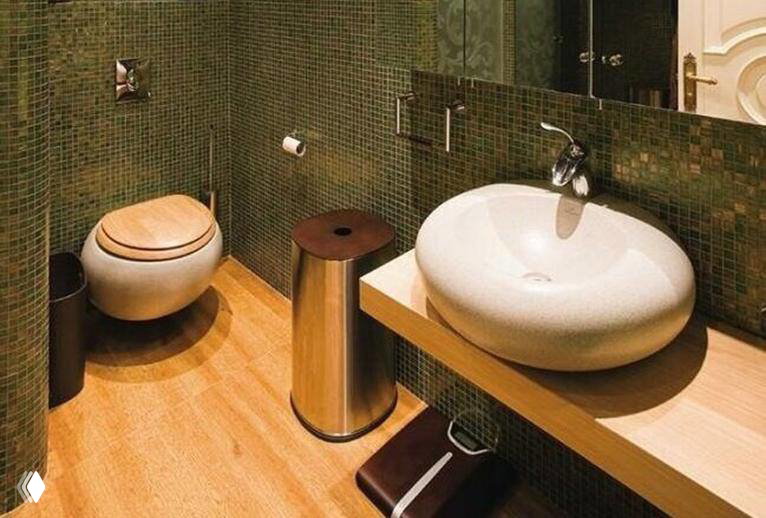 Ванная комната с мозаичной отделкой зелёных тонов, округлой раковиной и подвесным унитазом; отделка создаёт атмосферу, напоминающую природную, лесную палитру.