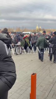 Толпа людей с букетами на площади у храма, дождливое пасмурное небо и силуэты собравшихся — сцена с прощания в Москве.