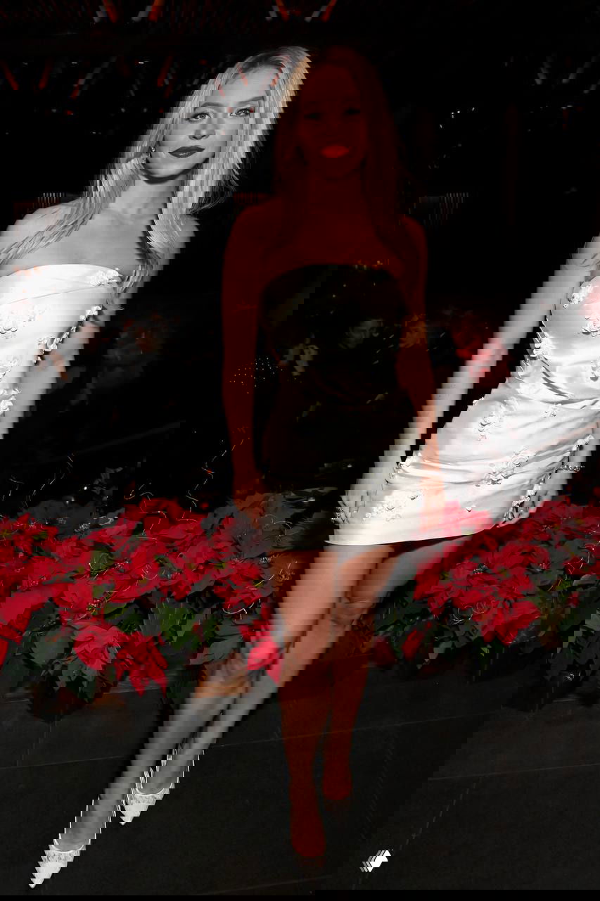 Сидни Суини в коротком белом платье с цветочными аппликациями, снята в вечерней обстановке у праздничных декораций