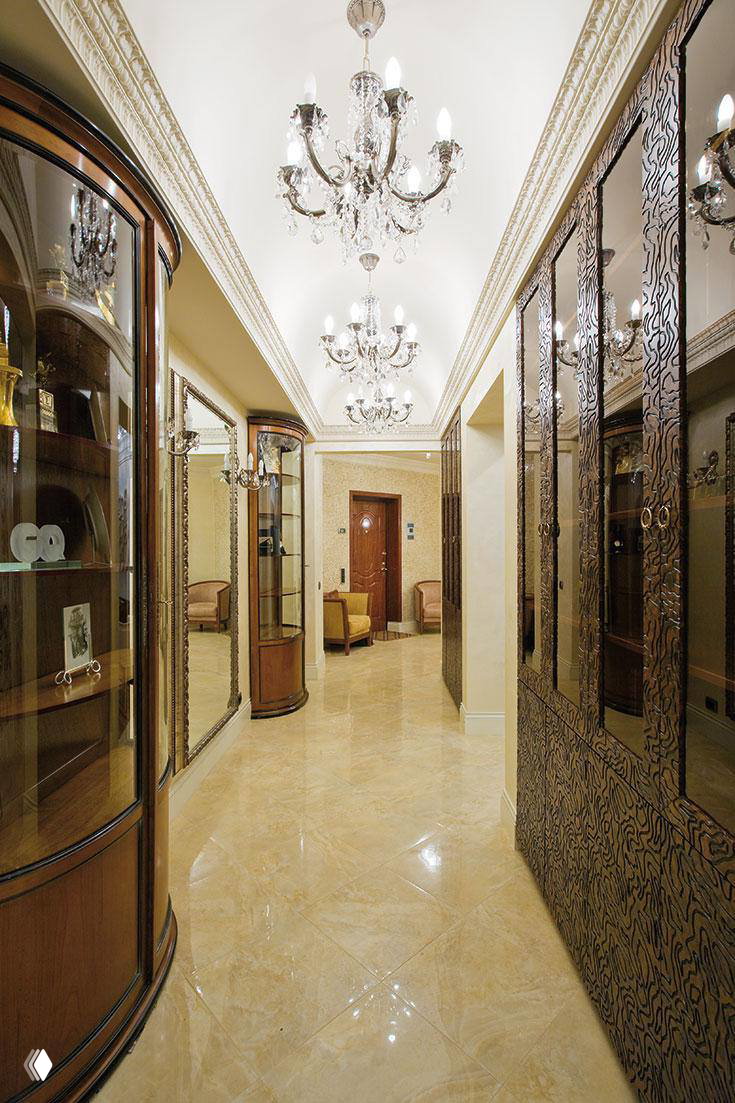 Широкий холл с полированным мраморным полом, зеркальными витринами и несколькими хрустальными люстрами; классический роскошный декор в деталях коридора.