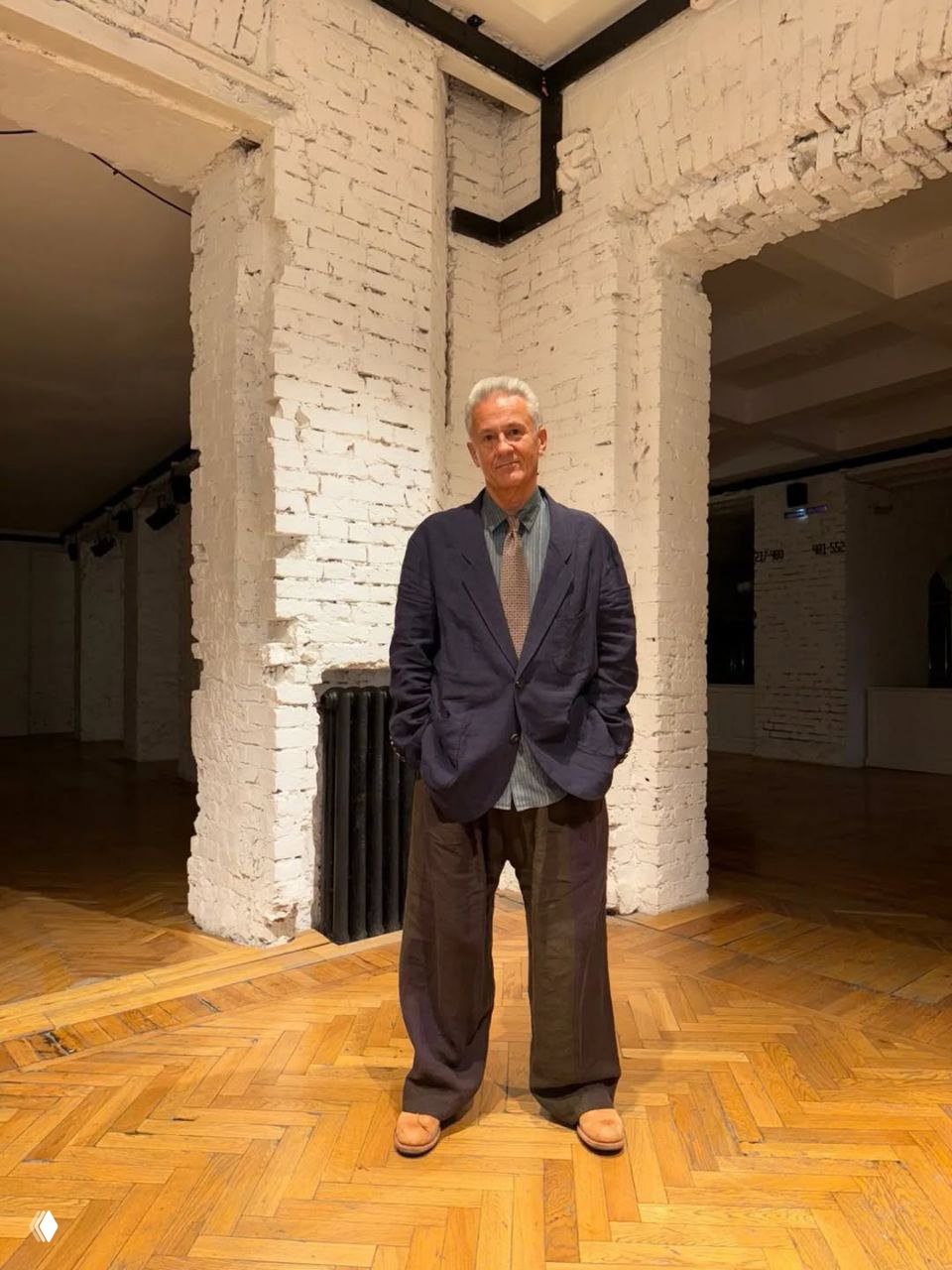 Классический мешковатый костюм: тёмный пиджак, свободные брюки и бежевые туфли — спокойный классический образ в галерейном пространстве.