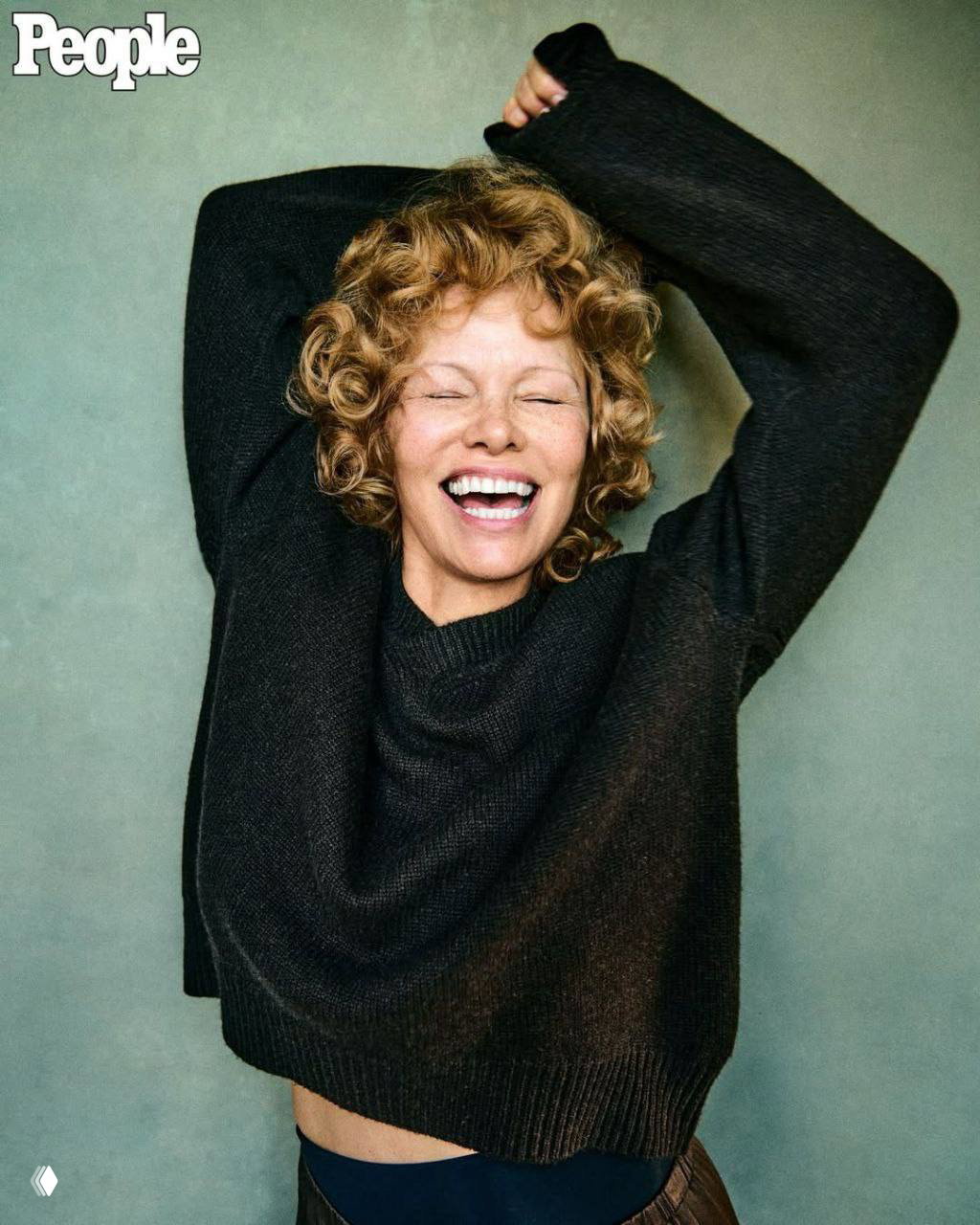 Памела Андерсон смеется в черном свитере на нейтральном фоне, непринужденная поза, без макияжа, кадр из фотосессии People.