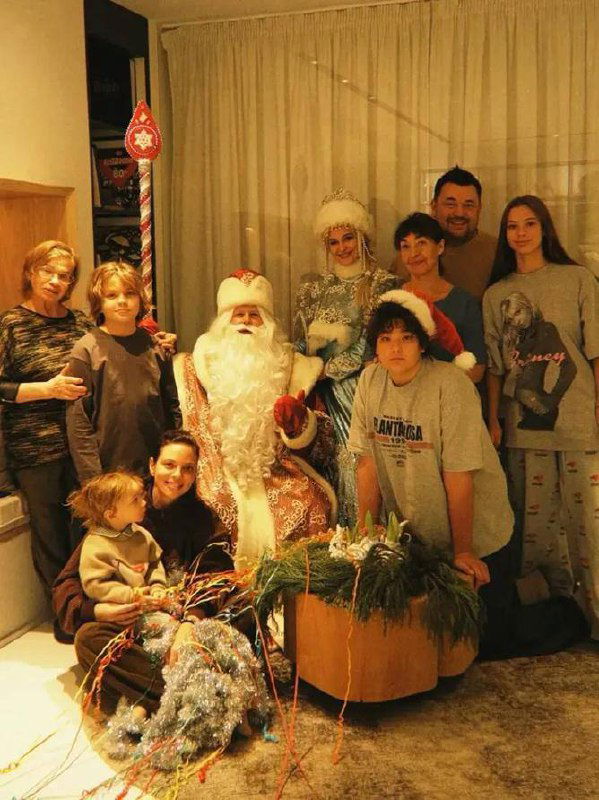Семейное фото с Дедом Морозом и Снегурочкой: большая компания родственников разного возраста собралась дома для празднования Рождества, тёплая домашняя обстановка