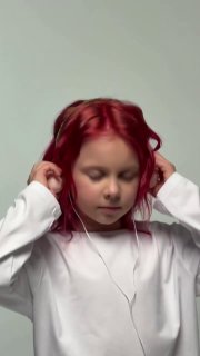 Фото 8‑летней дочери блогеров Дениса и Елены Кукояк с ярко‑красными покрашенными волосами, в белой рубашке и наушниках на нейтральном фоне, портрет