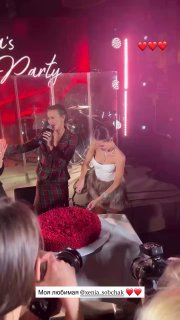 Ведущая на сцене и именинница у торта, сценическая подсветка и камеры в кадре, праздничная обстановка.