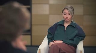 Кадр из студийного интервью: сидящий человек в кресле в тёмно-зелёной кофте на нейтральном фоне, разговорный формат, крупный план, спокойная поза.