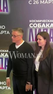 Алексей Макаров и жена Полина на премьере «Космическая собака Лида», фон с постером и логотипом Woman.ru, рядом микрофоны