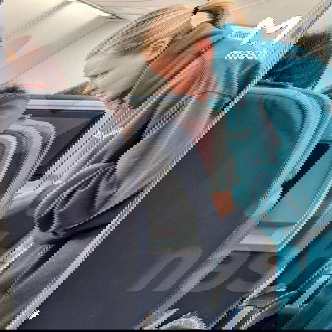 Снимок внутри салона самолёта: пассажирка в тёмно‑зелёном худи наклоняется над креслом, видны сиденья и бортовой интерьер.